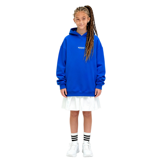 A girl wearing the Klein blue hoodie dress layered over a white skirt, showcasing its versatile oversized fit.