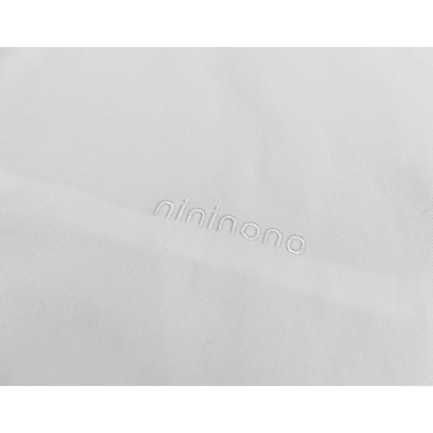 Detailed shot of the subtle white "nininono" embroidery on the left chest of the white shirt.