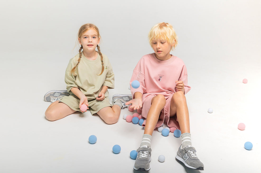Two children playing with colorful balls; a boy in a soft pink oversized sweatshirt and a girl in a light sage green set, demonstrating ØGENDER’s belief that colors represent personal energy rather than gender.