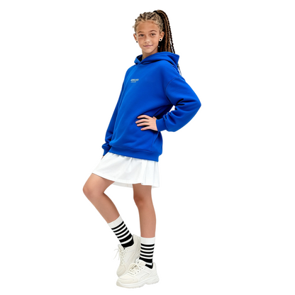 A girl wearing the Klein blue hoodie dress layered over a white skirt, showcasing its versatile oversized fit.