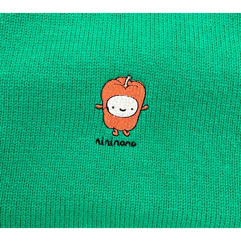 Detailed shot of the playful red pepper embroidery patch stitched on the chest of the green cardigan.