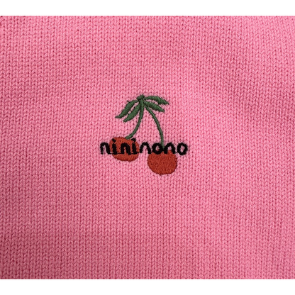 Detailed shot of the playful cherry embroidery patch stitched onto the chest of the pink cardigan.