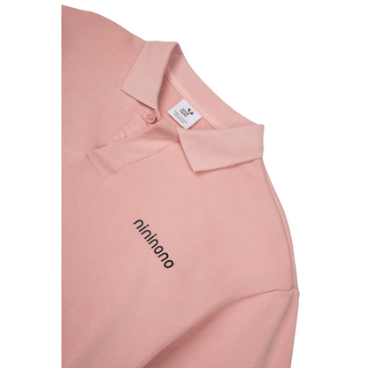 Close-up of the polo collar and button placket with subtle "nininono" branding on the pink fabric.