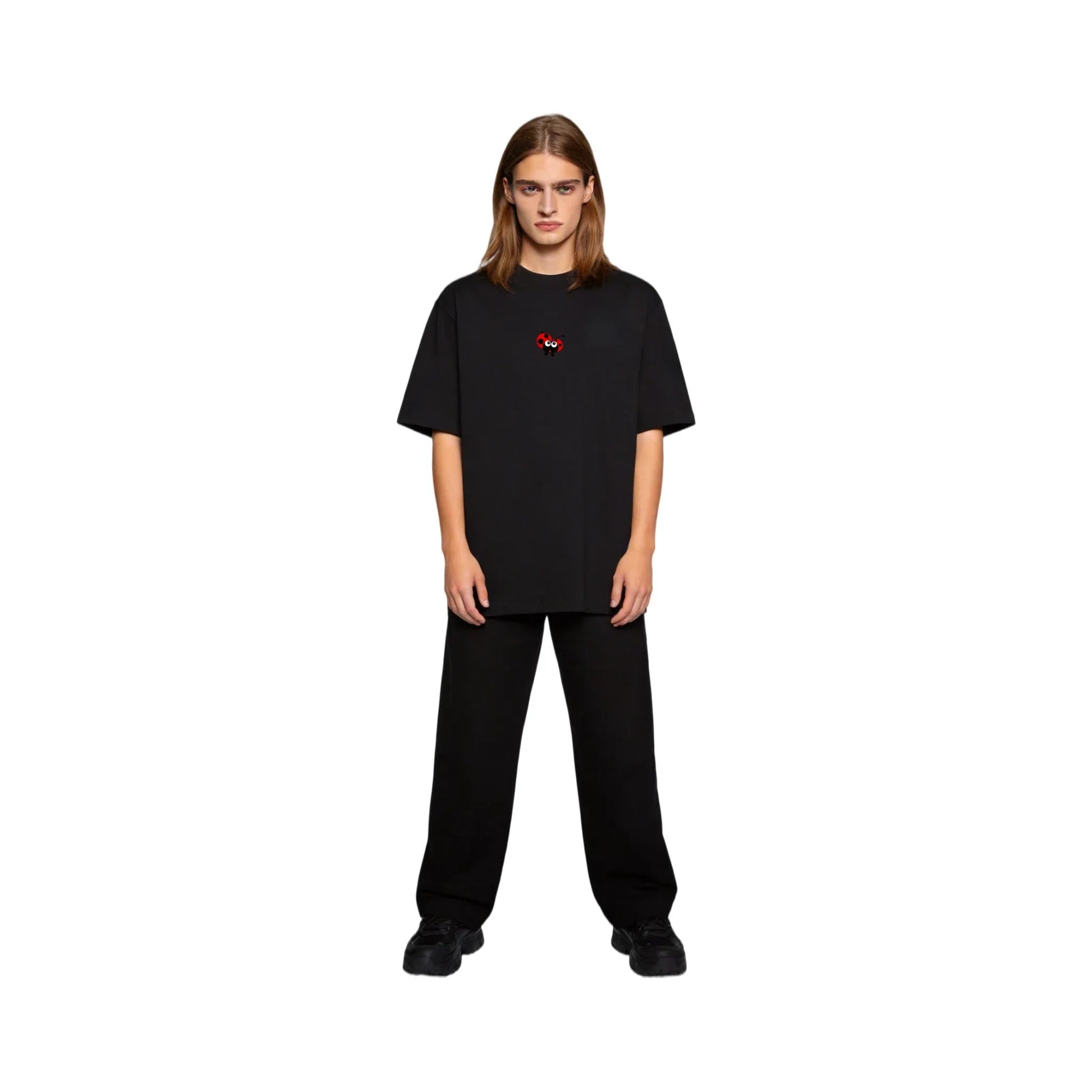 Full-body shot of a long-haired male model wearing the Ogender black 240 GSM ladybug tee and black jeans. Showcases the oversized unisex fit and minimalist red ladybug chest print for teens and adults