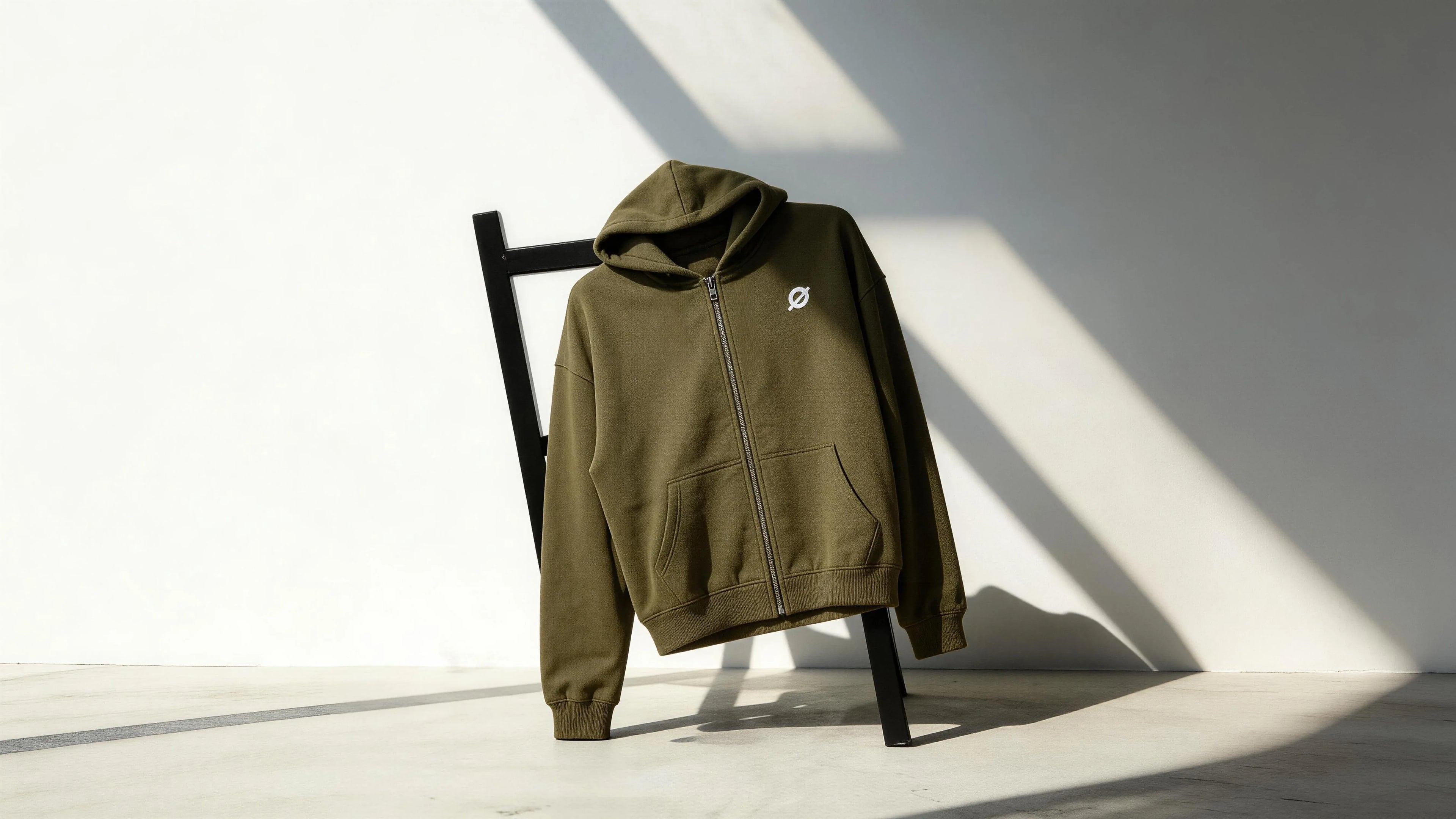 OGENDER 345g heavy fleece zip-up hoodie in sage green with a minimalist white logo, draped over a black chair in cinematic lighting