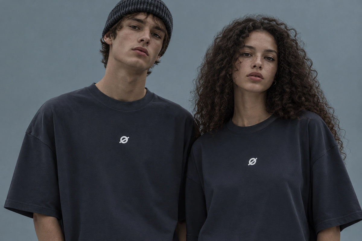 OGender dark gray oversized T-shirts with a white Ø logo, modeled by a young Russian man wearing a knit beanie and a young Russian woman against a cool-toned studio background.