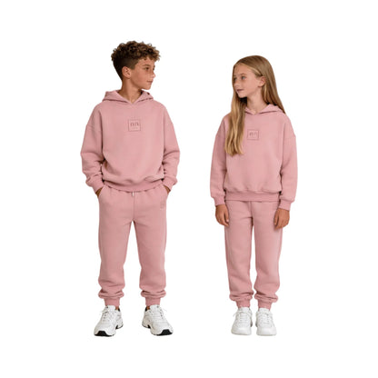 A boy and girl model wearing matching dusty pink hoodies and fleece-lined joggers.