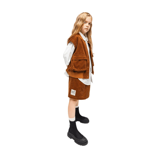 Full side profile of a girl modeling the caramel corduroy utility vest and skirt set.