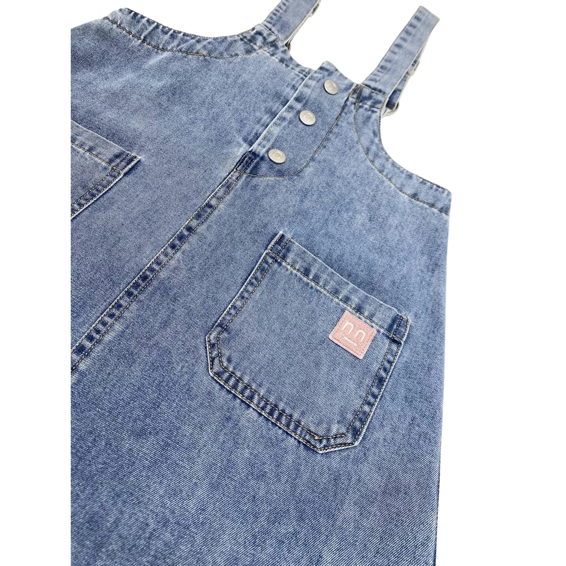 Close-up of the pink smiley embroidery on the left side pocket of the indigo denim dress.
