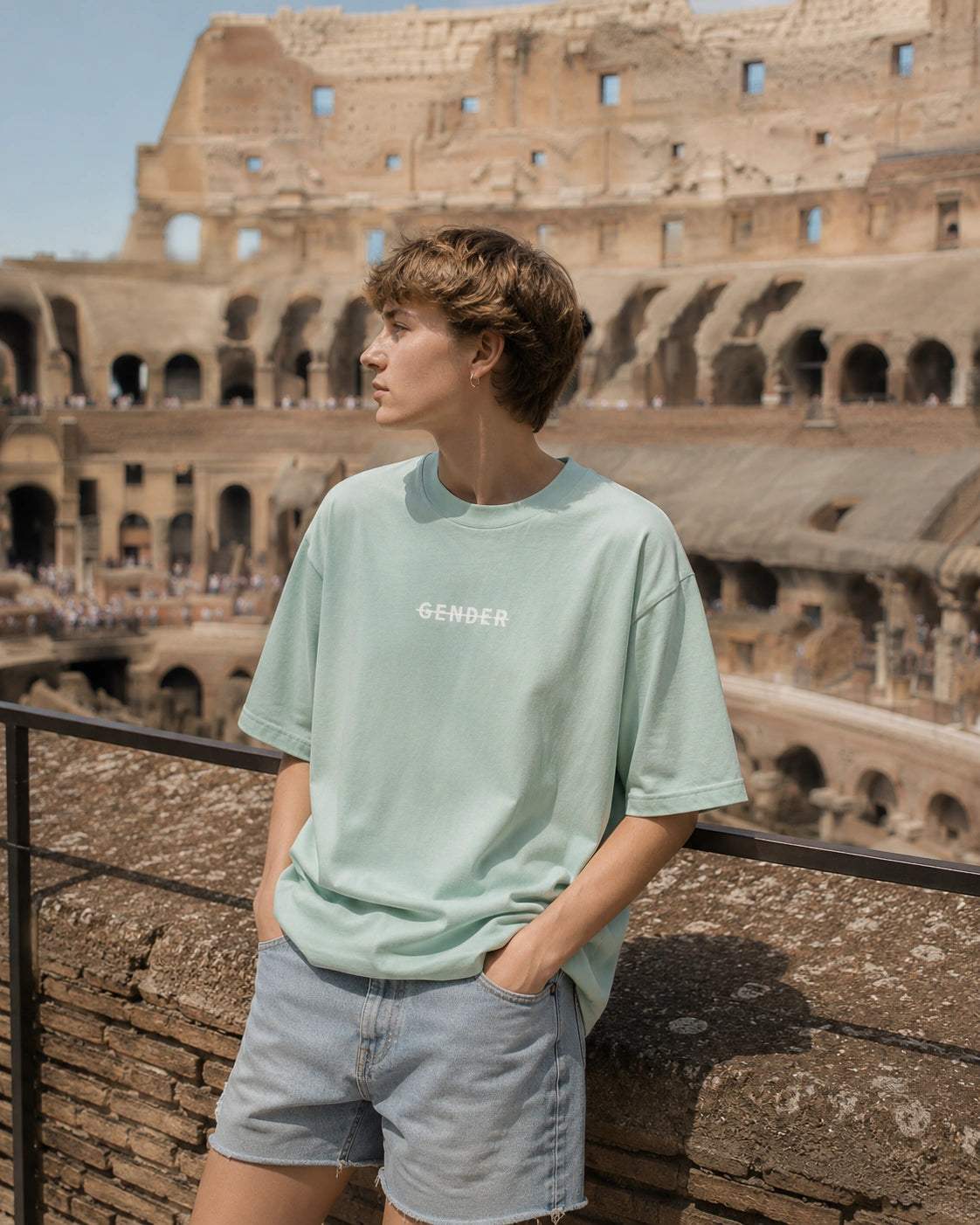 Androgynous Russian model wearing an oversized mint green tee and light blue denim shorts inside the Colosseum with a vacation-inspired style.