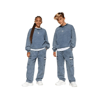 Full-body shot of a teenage boy and girl wearing the Ogender unisex oversized denim pullovers paired with matching vintage washed denim cargo pants for a coordinated streetwear look.