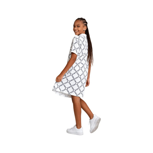 A young girl modeling the white all-over logo print polo dress showing the sporty side slit detail.
