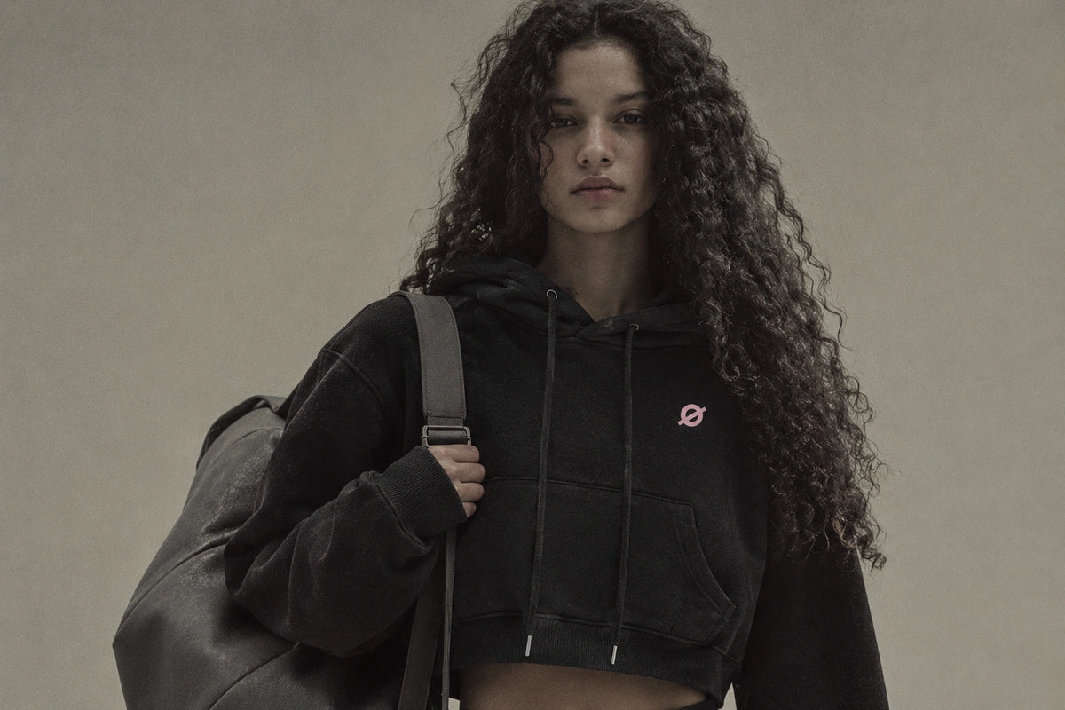 OGender black fleece-lined cropped hoodie with a small pink Ø logo, worn by a young female model against a muted neutral background.